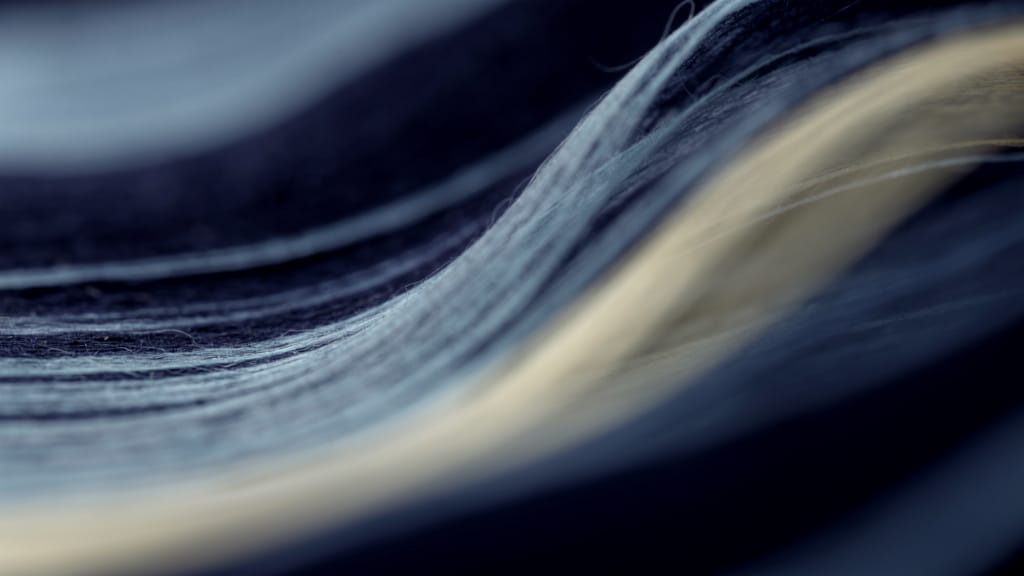 Abstract macro texture of soft long-exposure streaks of pale blue and faint yellow light drifting across a deep navy dar