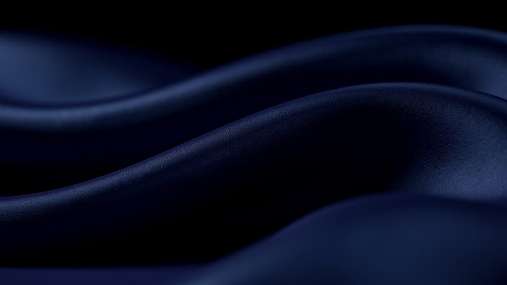 Abstract macro texture of deep indigo silk fabric in soft rolling folds catching a faint cool blue light on a near-black